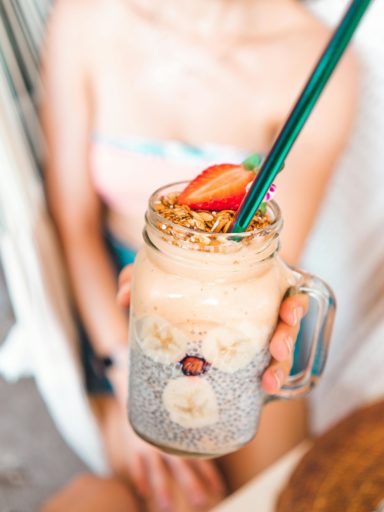 Person holding chia seed smoothie drink in mason jar with turquoise metal straw